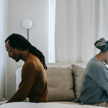 Man en vrouw zitten op bed met de ruggen naar elkaar toe, omdat ze een conflict hebben.